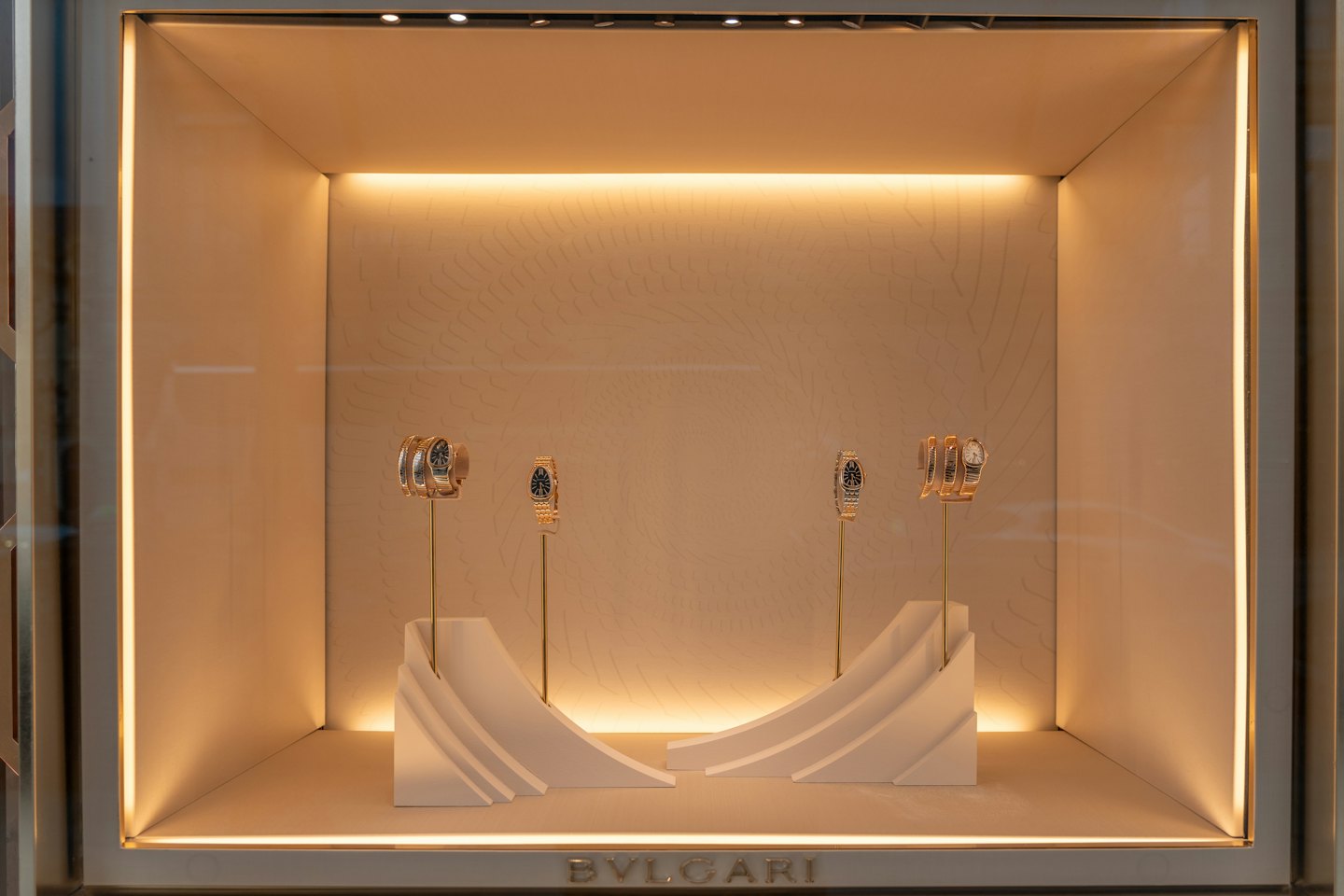 Four luxury watches displayed on golden stands inside a jewelry case.