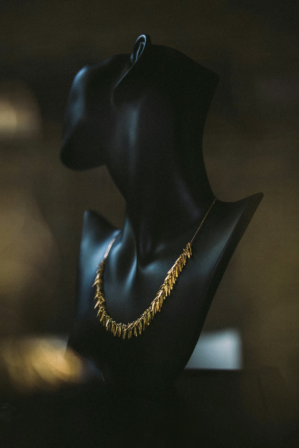 Gold necklace with leaf pendants displayed on a black mannequin.