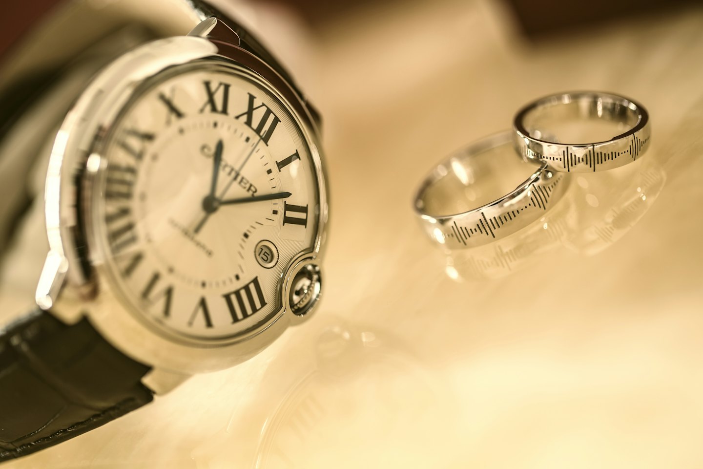 Luxury Cartier watch and engraved wedding bands on a golden surface.