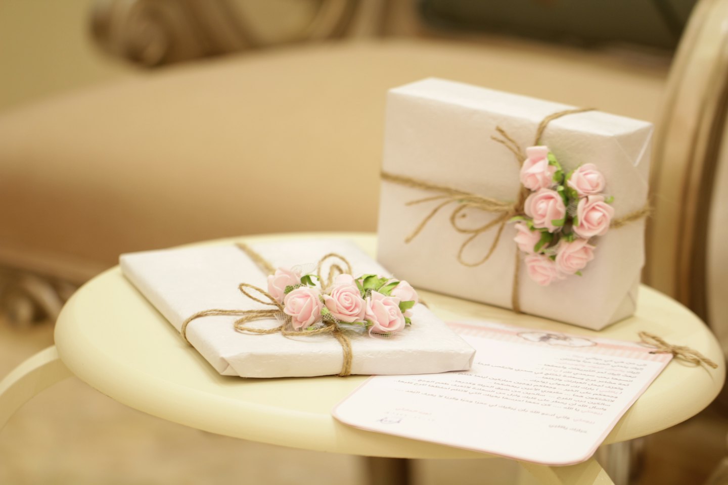 Two white wrapped gifts with pink roses on a light yellow table.