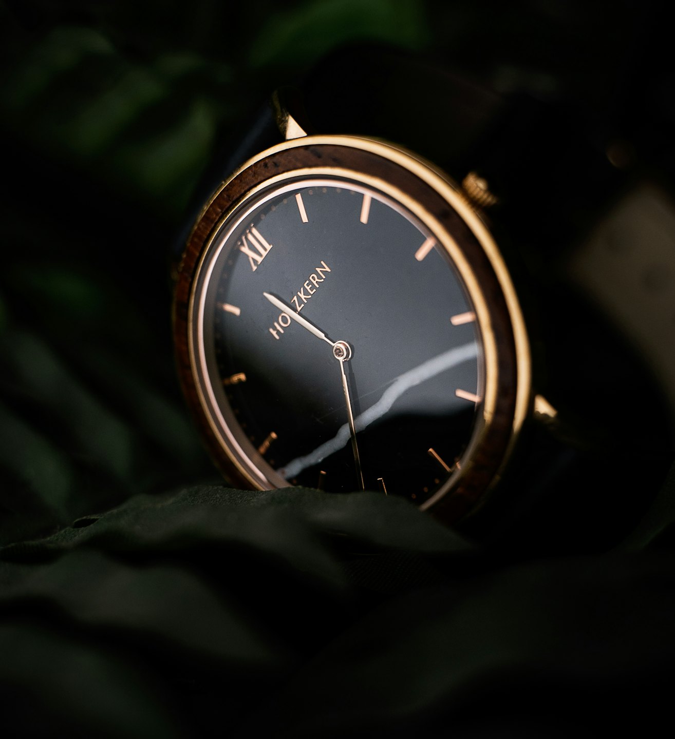 Rose gold wristwatch with black dial on dark green fabric.