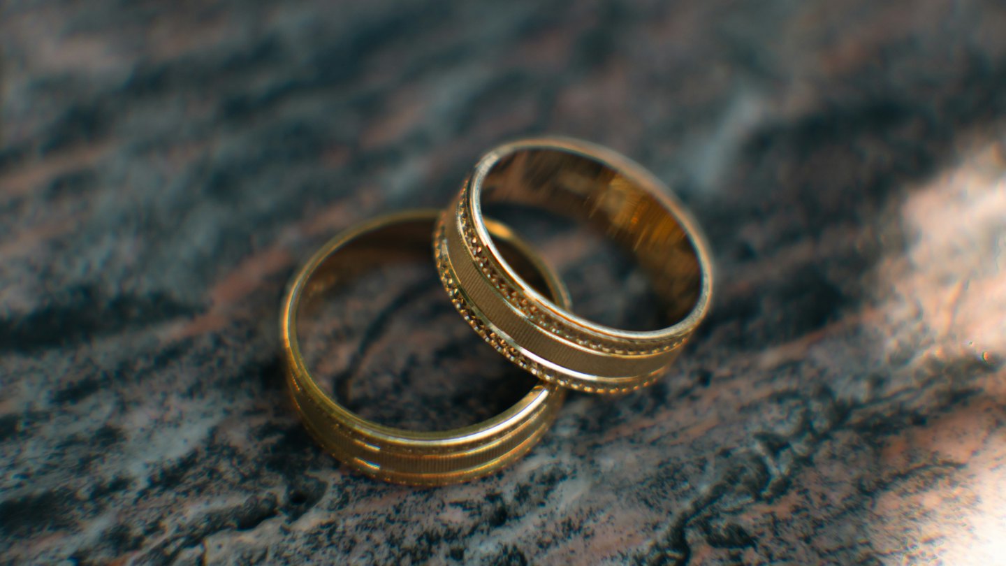Two gold wedding rings rest on a mottled marble surface.